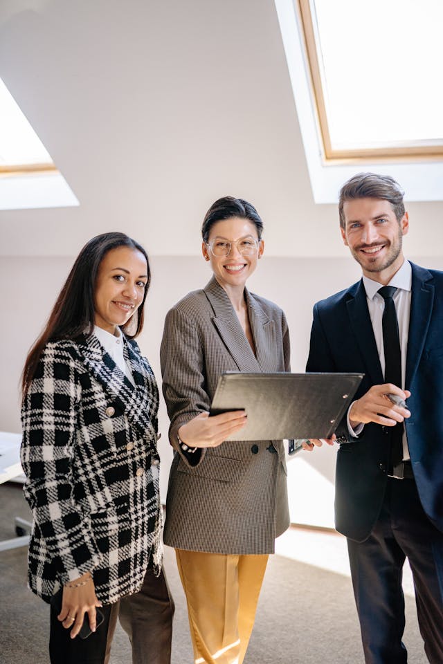Dans un bureau lumineux, trois professionnels en tenue d’affaires échangent autour d’une tablette, illustrant une collaboration de partenaires.
